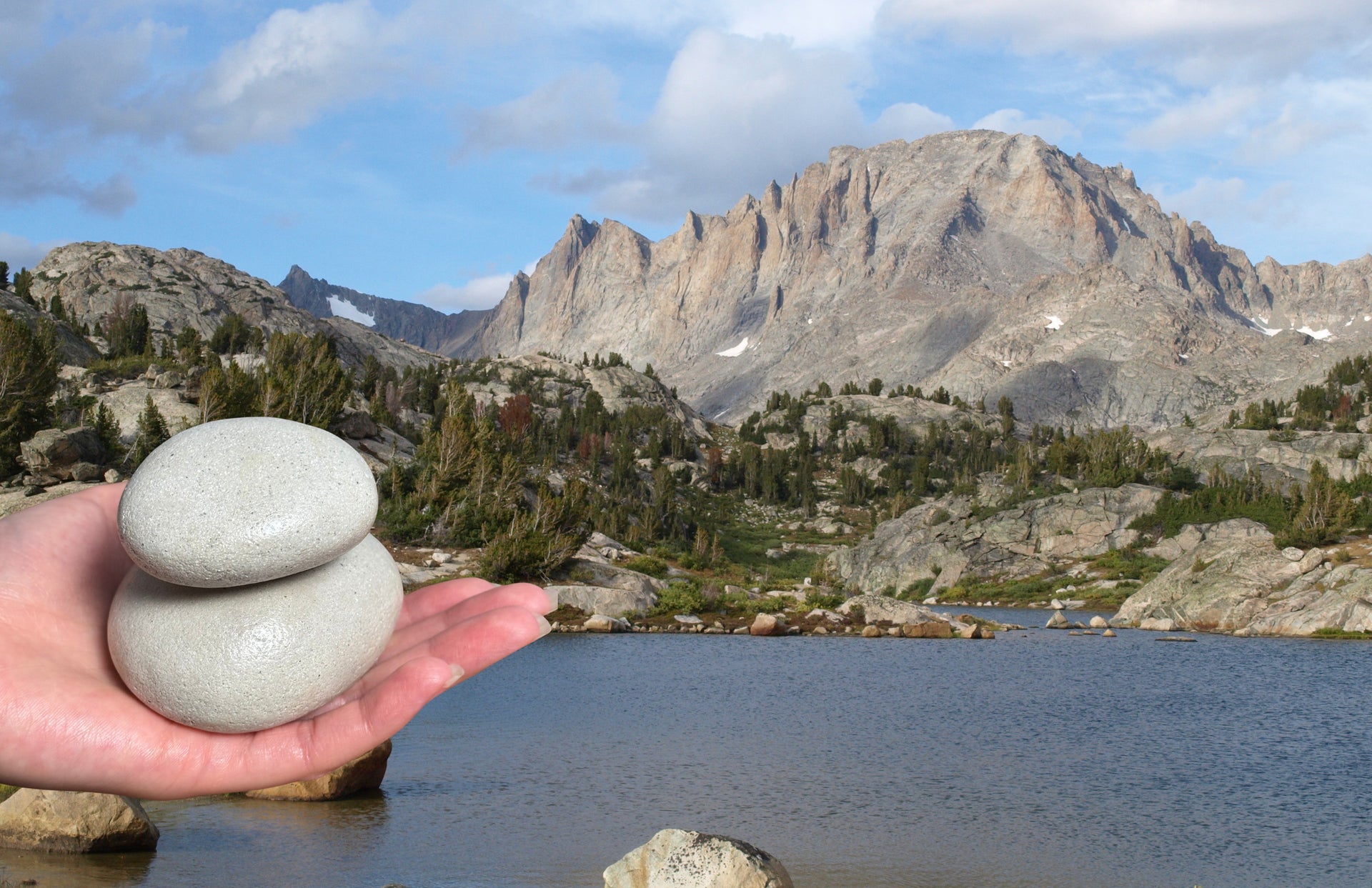 Hand holding two stones with a mountainous landscape in the background