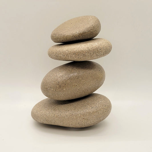 Stack of cremation memorial stones - stones are made from cremated ashes of departed loved one. Four stones stacked on in a cairn formation against a white background.